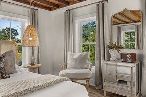 Un dormitorio con cama, una silla, un tocador, un espejo y una lámpara.