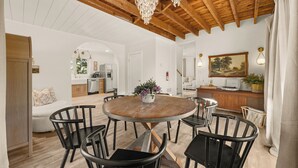 A spacious dining area with a round wooden table surrounded by chairs, a chandelier above, and a painting on the wall.