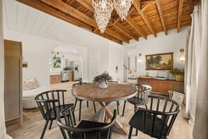 Un comedor amplio con una mesa redonda de madera rodeada de sillas, un candelabro encima y un cuadro en la pared.