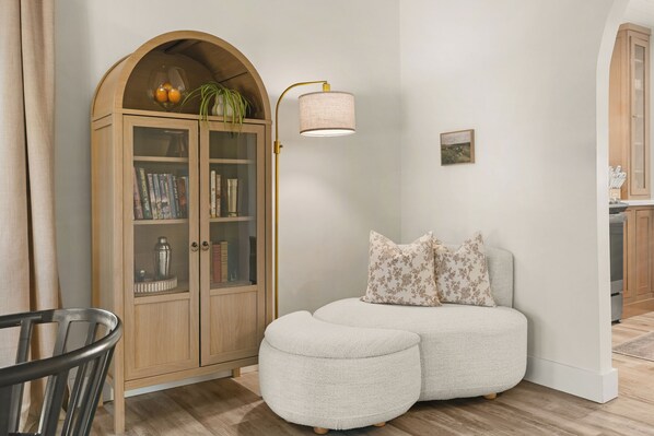 A room with a wooden arched cabinet, a white sofa with floral cushions, and a wall-mounted lamp.