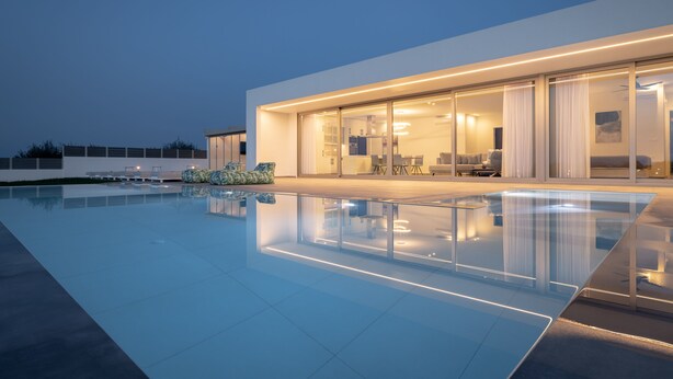 Una casa moderna con piscina, puertas de cristal amplias y un interior bien iluminado.