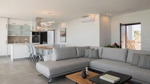 Una sala de estar moderna con un sofá seccional gris, una mesa de centro de madera y un comedor con una mesa y sillas blancas.