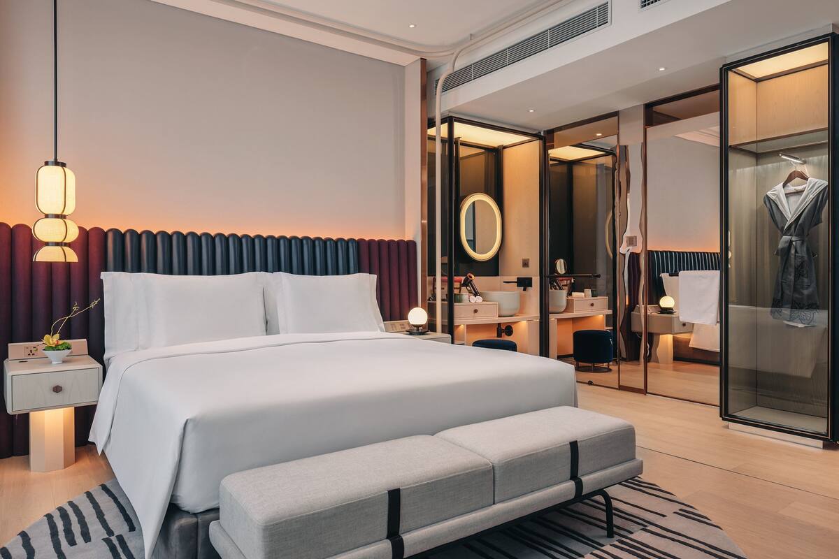 Ein modernes Hotelzimmer mit einem großen Bett, einem Nachttisch und einem begehbaren Kleiderschrank mit Spiegel.