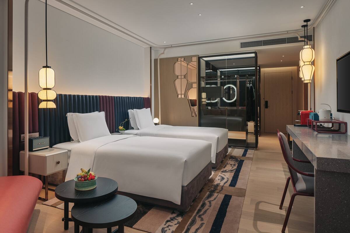 Ein Hotelzimmer mit zwei Betten, einem Schreibtisch, einem Stuhl, einem kleinen Tisch und einem roten Sofa.