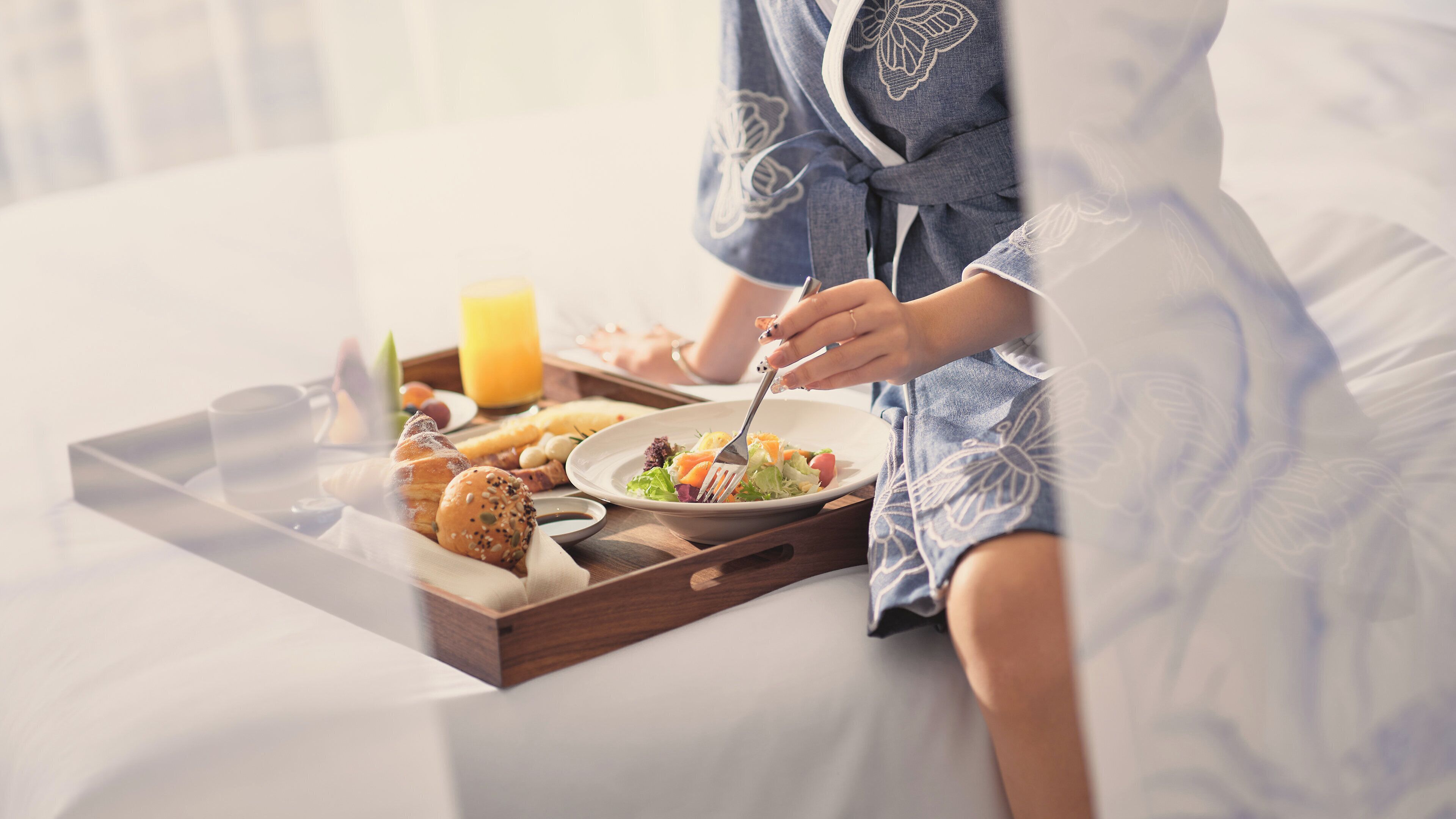 A breakfast tray with croissants, a salad, and a glass of orange juice on a bed.