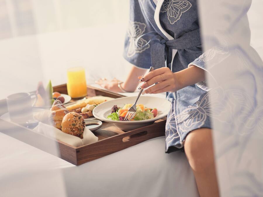 A breakfast tray with croissants, a salad, and a glass of orange juice on a bed.
