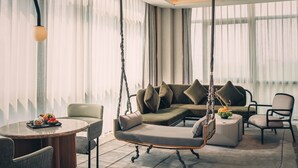 Un salon moderne avec un fauteuil suspendu, un canapé avec des coussins, une table ronde sur laquelle est disposé un plateau de fruits et une plante en pot.