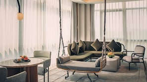 Un salon moderne avec un fauteuil suspendu, un canapé avec des coussins, une table ronde sur laquelle est disposé un plateau de fruits et une plante en pot.