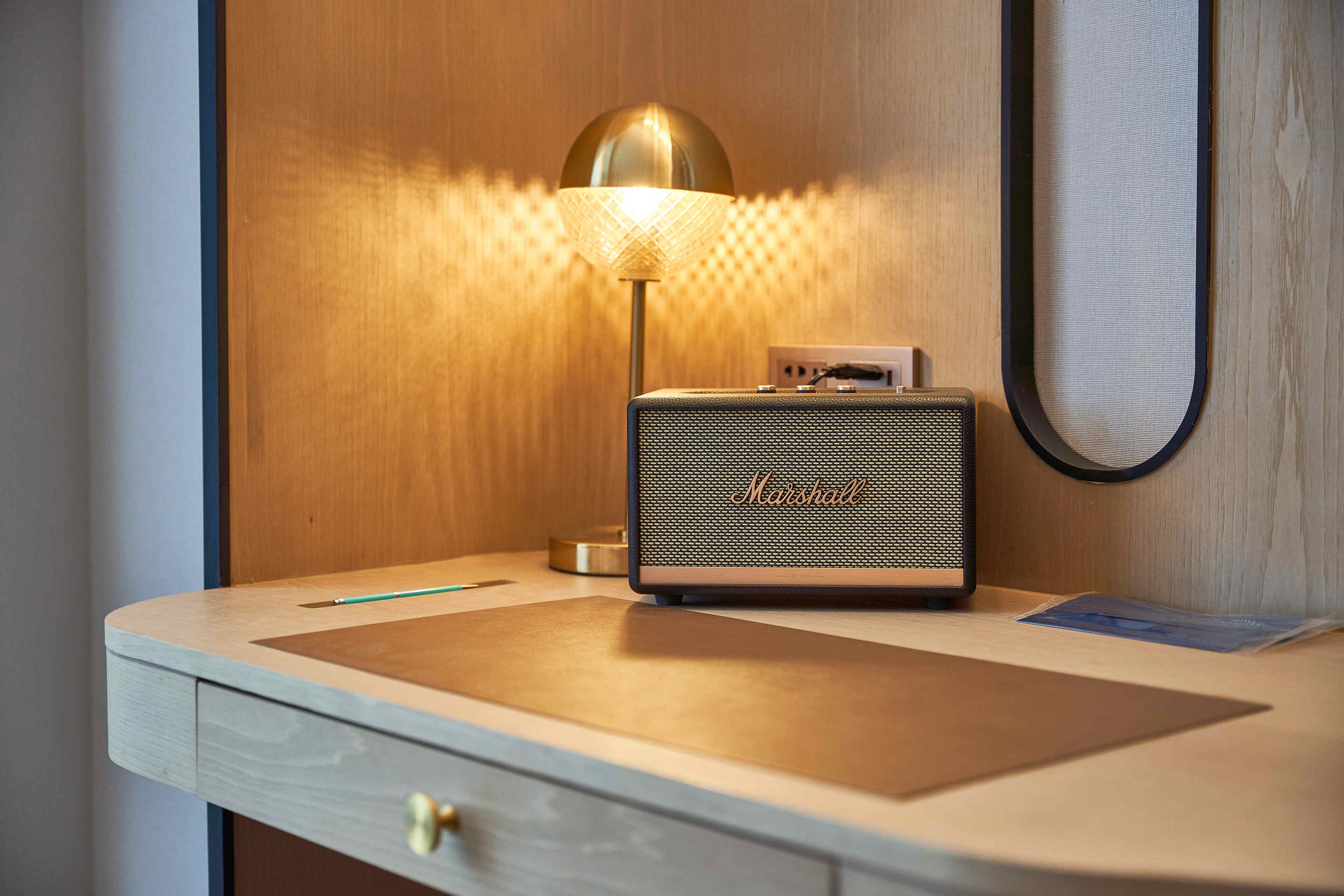 Un escritorio de madera con un altavoz Marshall antiguo, una lámpara y un cajón.