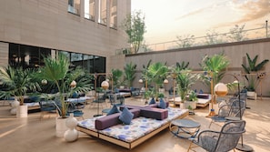 Un vaste espace extérieur aménagé avec de nombreux fauteuils et canapés confortables, entouré de plantes en pot et doté de grandes fenêtres.