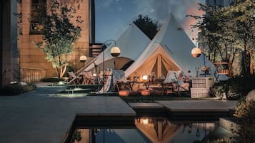 A tented outdoor area with seating and tables, surrounded by trees and a building.