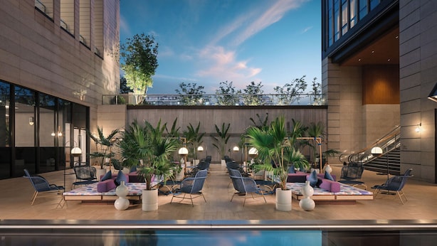 Un área de piscina en la azotea con sillones de descanso y plantas en macetas, rodeada de edificios modernos.