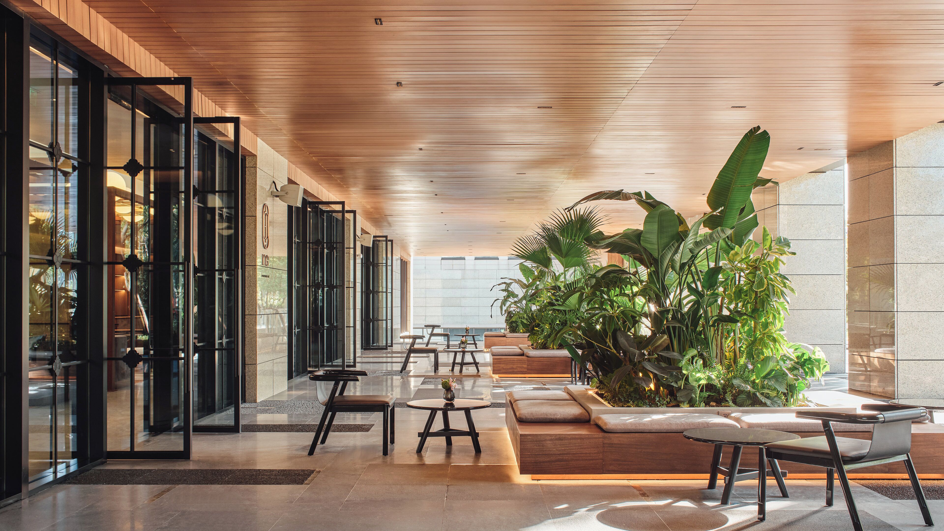 A modern indoor space with glass doors, wooden ceiling, and seating areas.