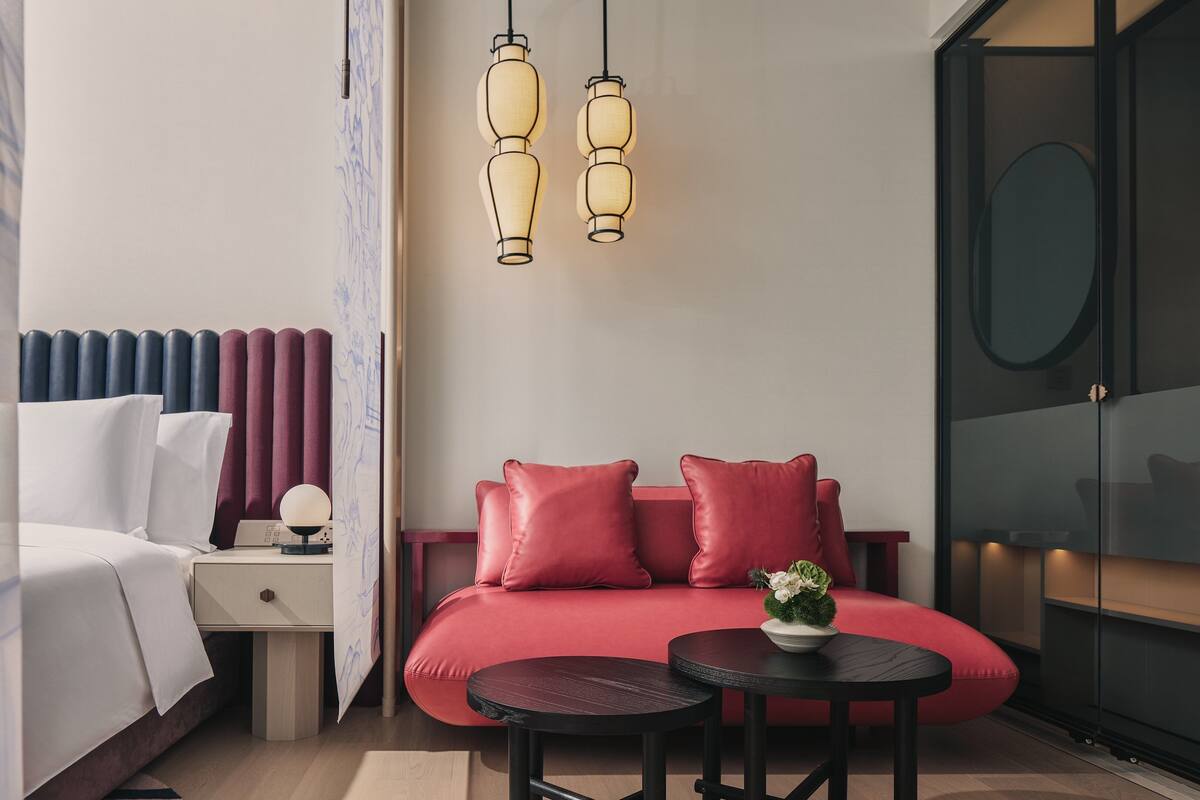 Ein modernes Hotelzimmer mit einem Bett, einer roten Couch, einem kleinen Tisch und einem Nachttisch.