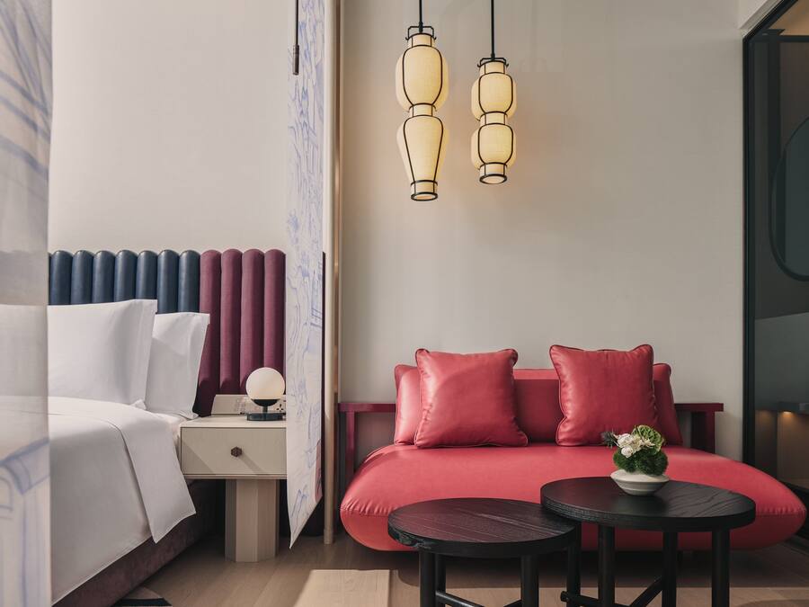 Moderni hotellihuone, jossa on sänky, punainen sohva, pieni pöytä ja yöpöytä.