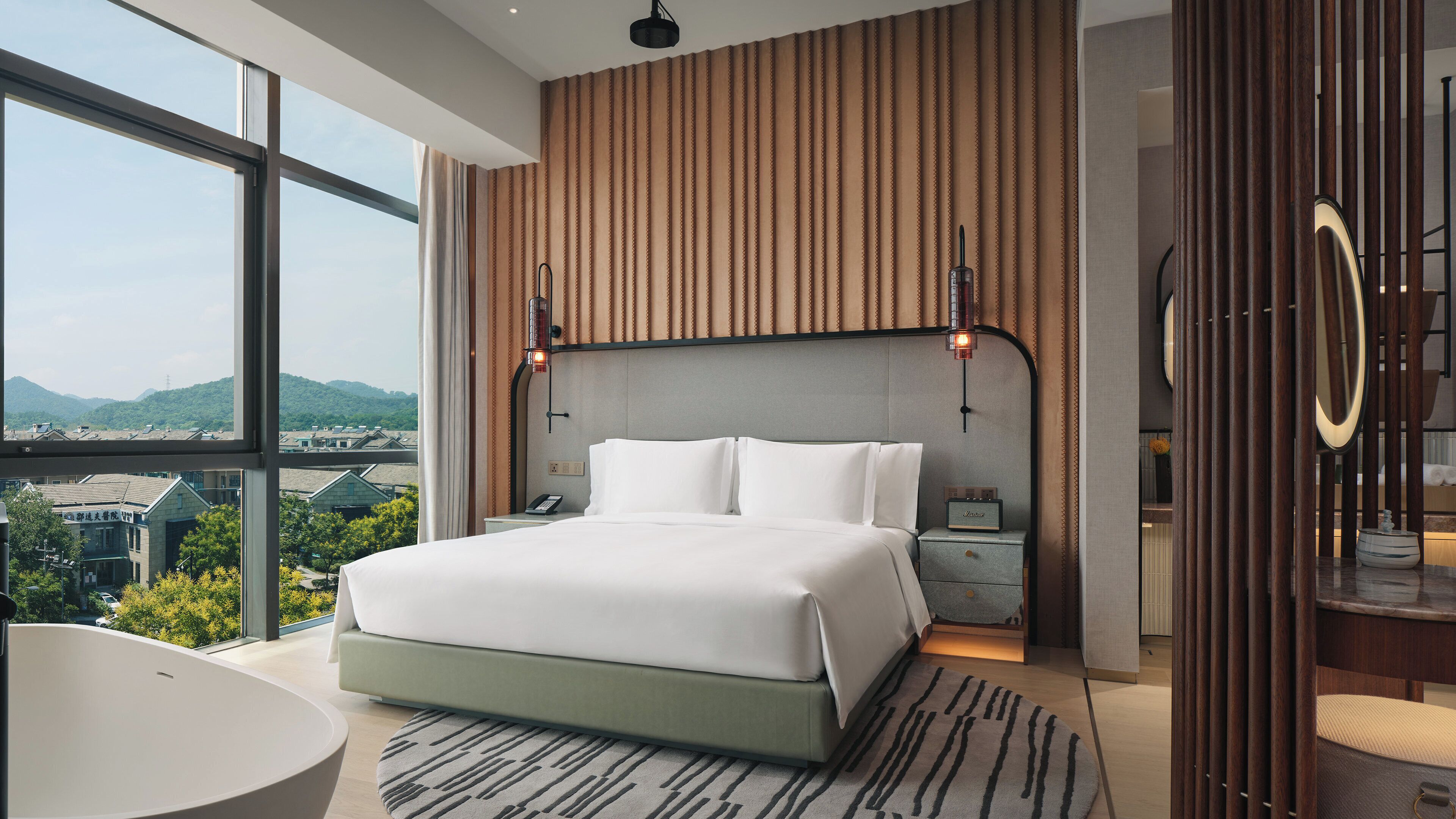 Een moderne hotelkamer met een groot bed, nachtkastje, bureau, stoel, bad en uitzicht op de stad.