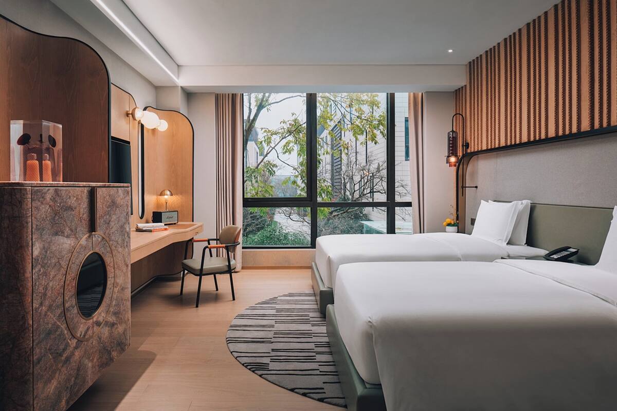 Ein Hotelzimmer mit Bett, Schreibtisch, Stuhl, Spiegel und einem großen Fenster.