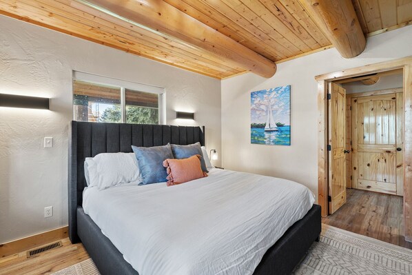 Ein Schlafzimmer mit einem Bett, einem Kopfteil, einem Gemälde und einer Holztür.