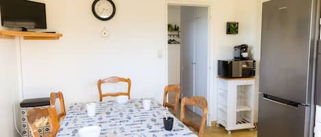 Un comedor con una mesa dispuesta para cuatro, un televisor arriba y un refrigerador a la derecha.