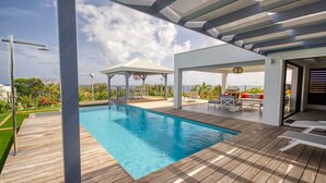 A wooden deck with a swimming pool, outdoor furniture, and a covered area with a view of the ocean. - Sea View Villa with Pool & Hot Tub - Sleeps 8 (Saint-François)