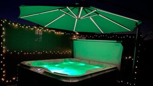 A hot tub with a green-lit interior, surrounded by string lights and under a green umbrella. - Stunning 3-bed Cottage in Lowestoft (Lowestoft)