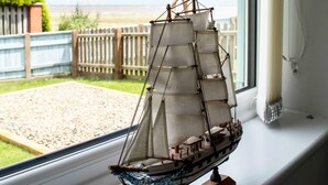 A model ship on a windowsill with a view of a beach and a wooden fence. - Stunning 3-bed Cottage in Lowestoft (Lowestoft)
