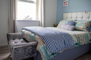 Une chambre à coucher avec une tête de lit capitonnée, une literie à rayures et un fauteuil capitonné.