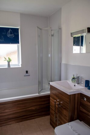 Ein modernes Badezimmer mit Duschkabine aus Glas, einem weißen Waschbecken und Holzschränken.