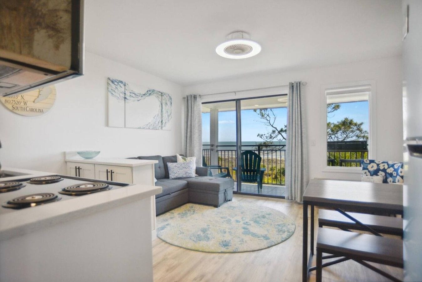 A modern kitchen with a dining area, a gray sofa, and a view of the outdoors.