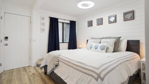 Quarto com cama, janela com cortinas, mesa de cabeceira e quadros na parede.