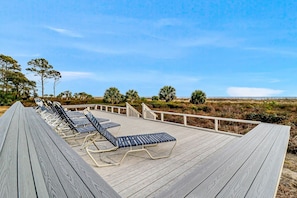 Une terrasse en bois, dotée de chaises longues et d’une rambarde offrant une vue sur un paysage naturel.