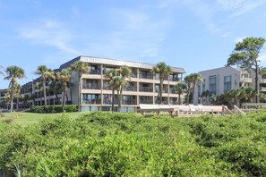 A multi-story hotel with balconies, palm trees, and a grassy area with lounge chairs.