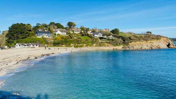 Una zona costiera con spiaggia sabbiosa, acque blu cristalline e case su una collina.