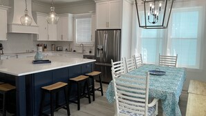 Een moderne keuken met witte kasten, een groot kookeiland, barstoelen en een eettafel met stoelen.