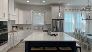 Een moderne keuken met witte kasten, roestvrijstalen apparatuur en een groot eiland met barkrukken.