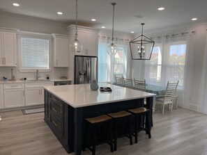 Enjoy dining or socializing at the central island with bar stools in this kitchen, featuring stainless steel appliances and a light wood floor.