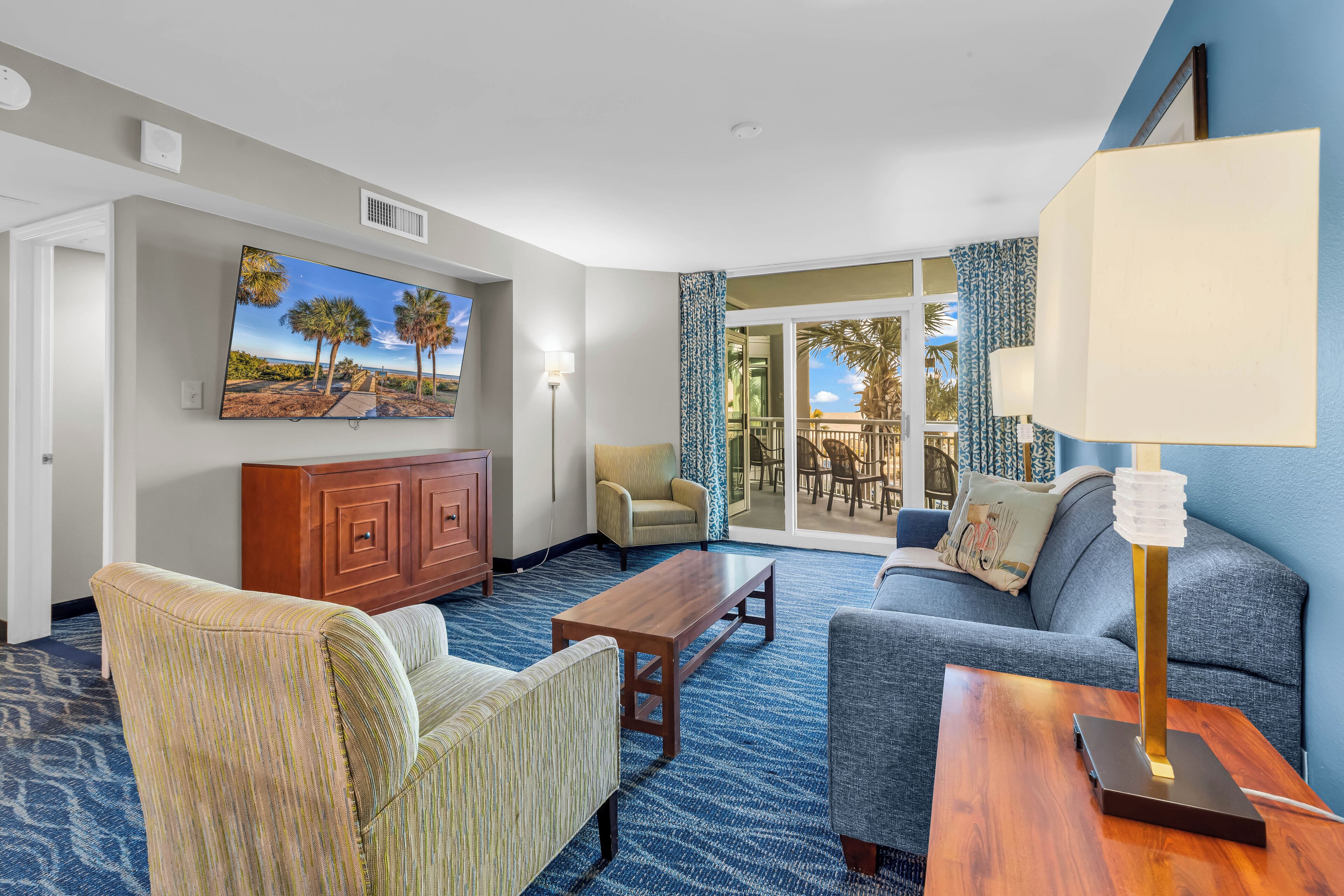 A hotel room with a large window, a sofa, a chair, a wooden coffee table, and a lamp.
