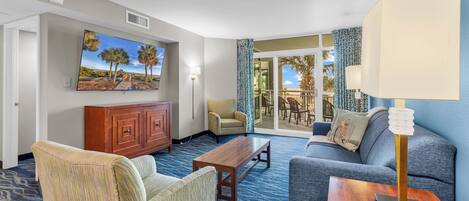 A hotel room with a large window, a sofa, a chair, a wooden coffee table, and a lamp.