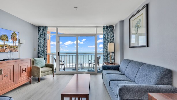 A modern living room with a grey sofa, a wooden coffee table, a beige armchair, and a TV on a wooden cabinet. - Dunes Village Resort by Hosteeva (Myrtle Beach)
