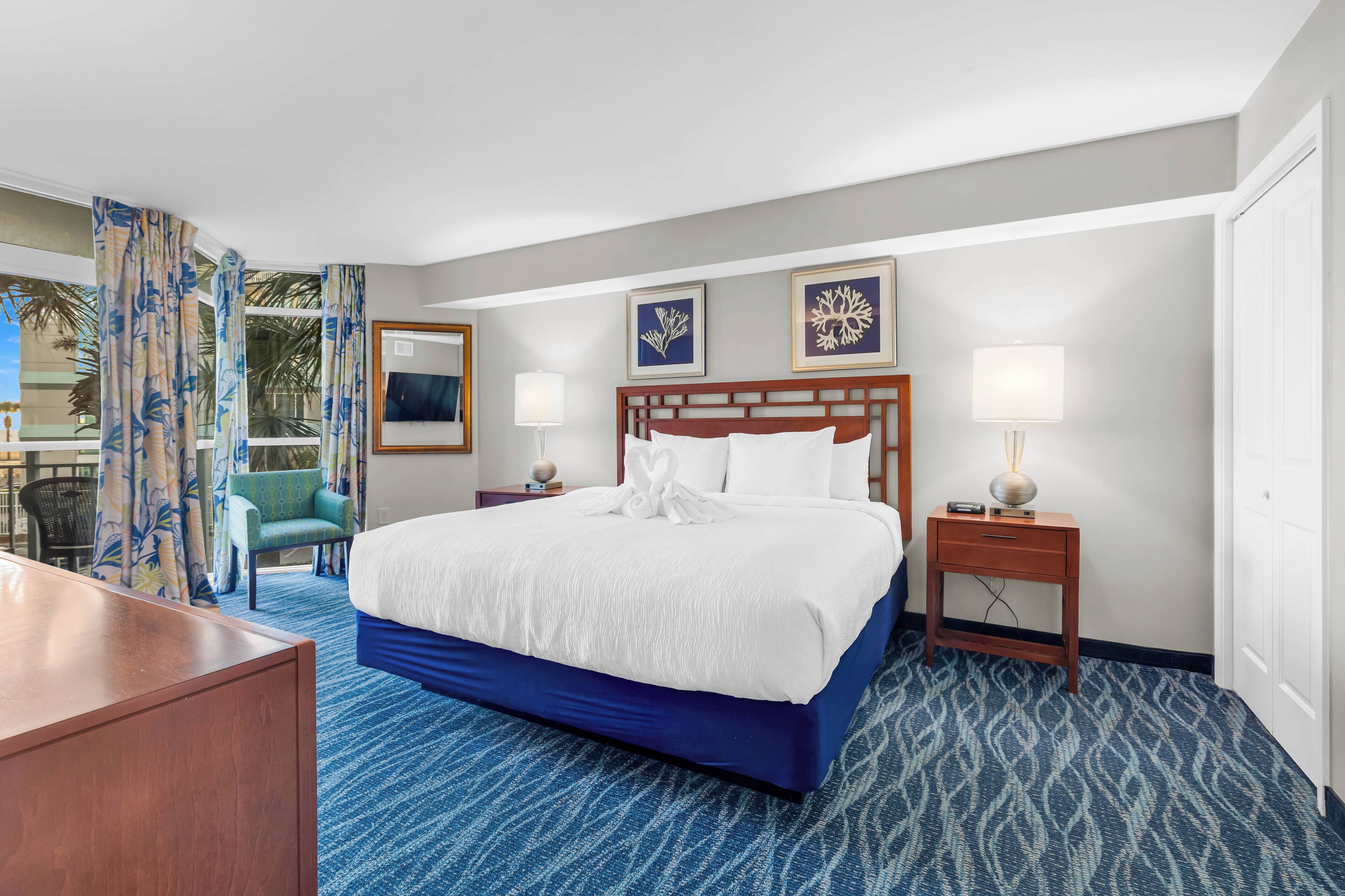 Een hotelkamer met een groot bed, twee nachtkastjes, een bureau en uitzicht op palmbomen.