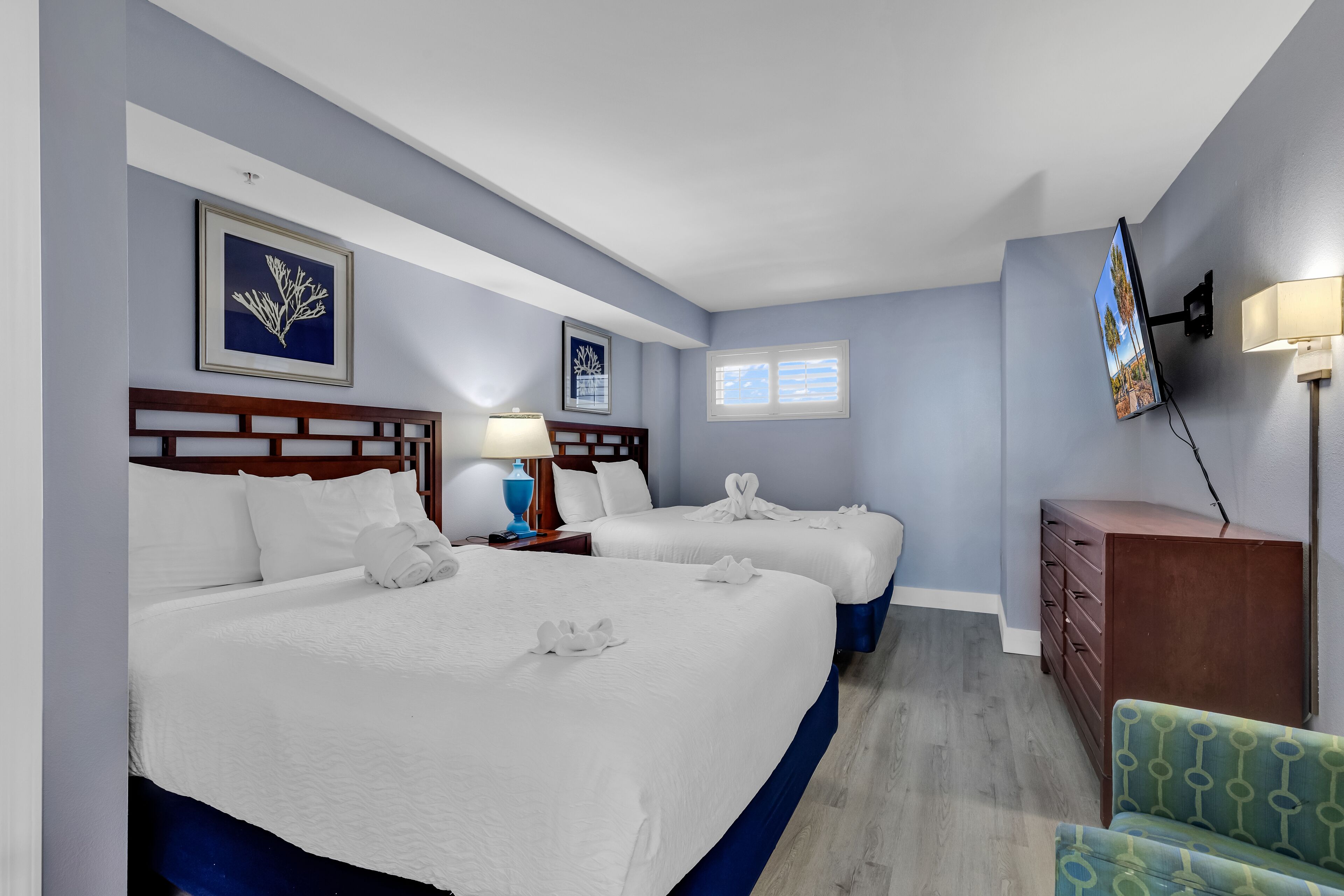 A hotel room with two beds, a TV, a dresser, and a chair.