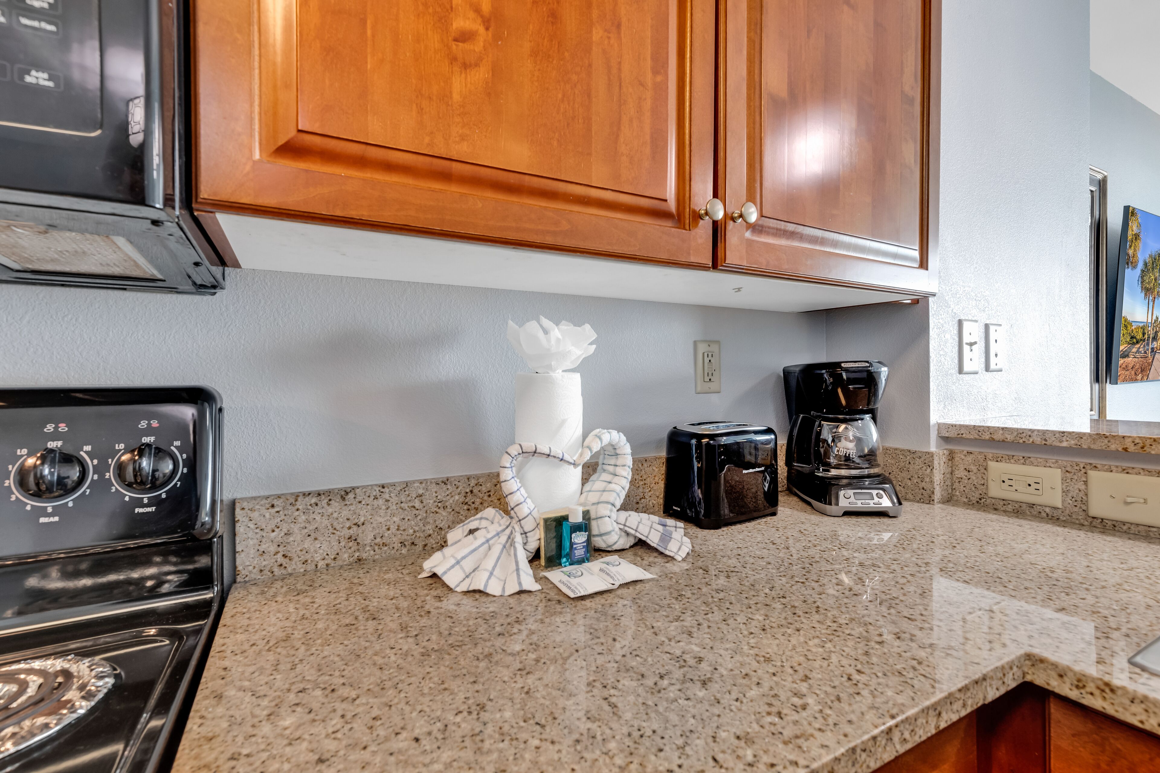 A kitchen with wooden cabinets, a stove, a coffee maker, and a bottle of hand sanitizer on the counter.