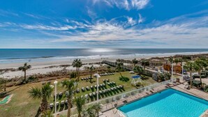 A pool area with lounge chairs, a clear view of the beach, and a sunny sky. - Dunes Village Resort by Hosteeva (Myrtle Beach)
