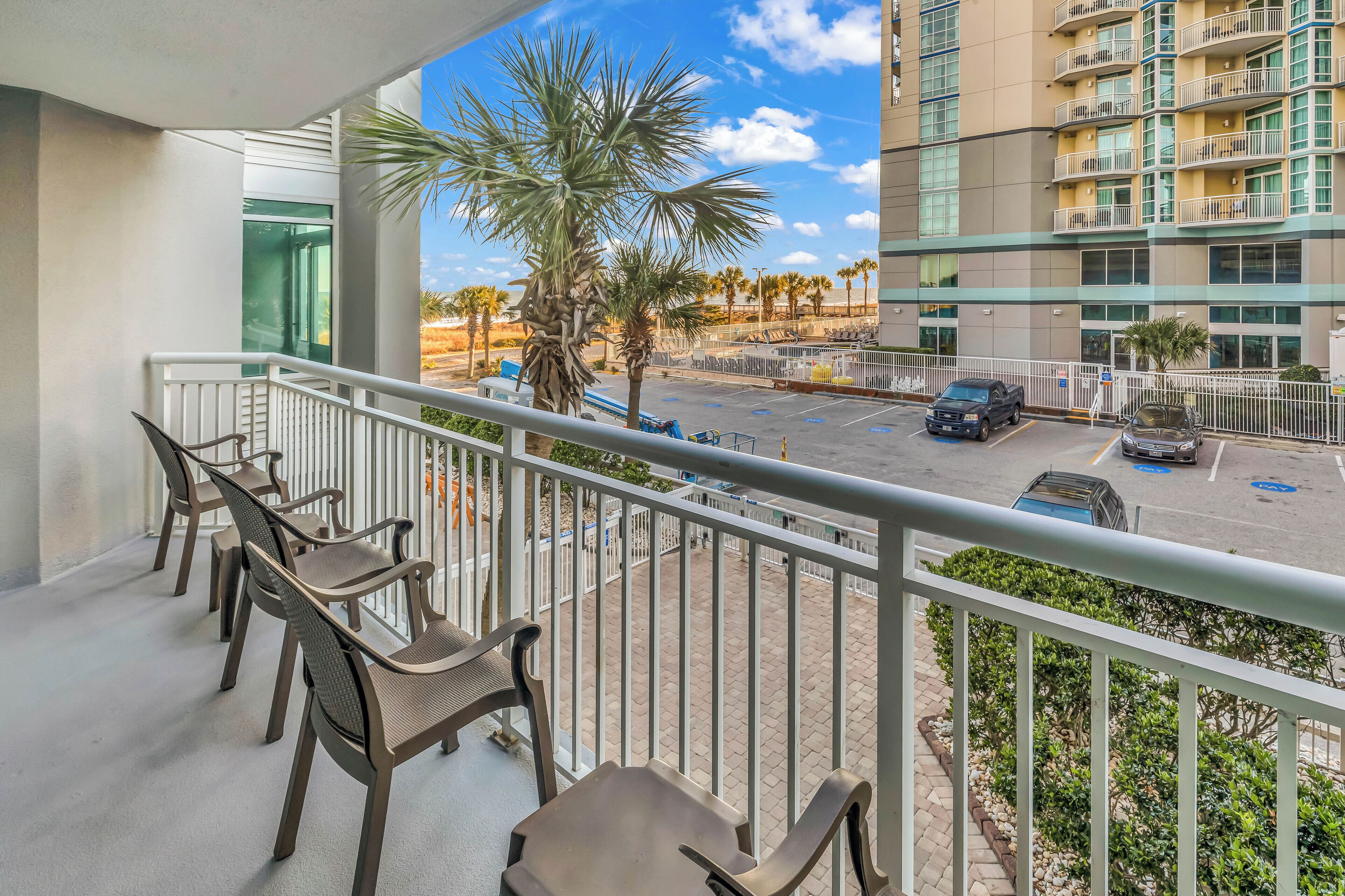 A balcony with seating and a view of a parking area and palm trees.