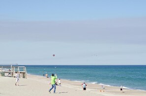 En strand med folk som leker, ett livräddartorn och havet.
