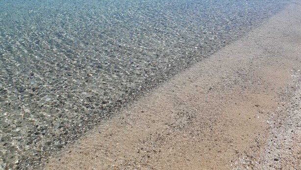 A clear beach with shallow water, pebbles, and distant hills. - The Broom (Golfo Aranci)