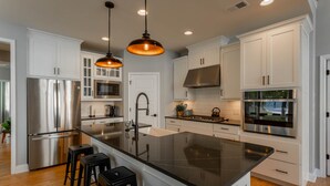 A modern kitchen with stainless steel appliances, white cabinetry, and black countertops.