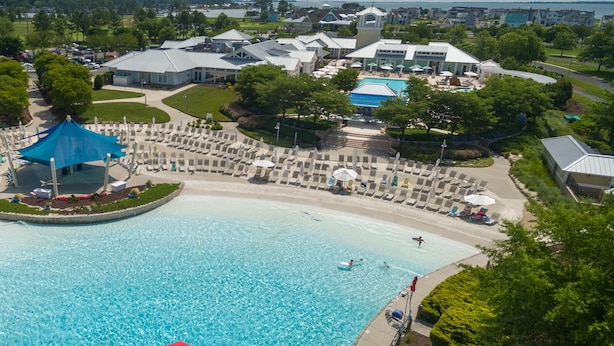 An aerial view of a resort with a large swimming pool, lounge areas, and a central building with a tower.