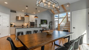 A spacious kitchen with a large wooden table, black chairs, and pendant lighting.
