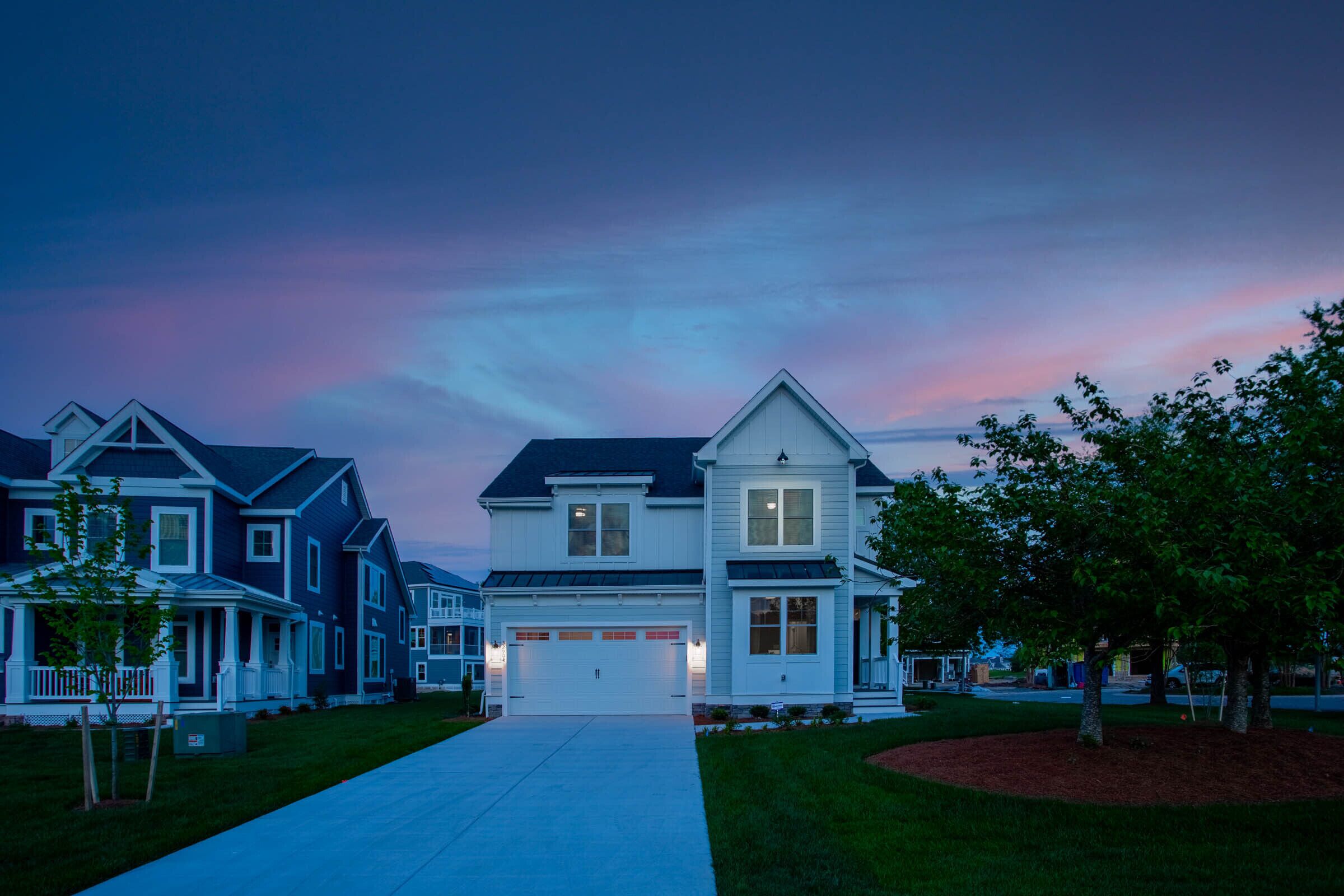 A suburban neighborhood with modern two-story houses, a well-maintained lawn, and a clear driveway.